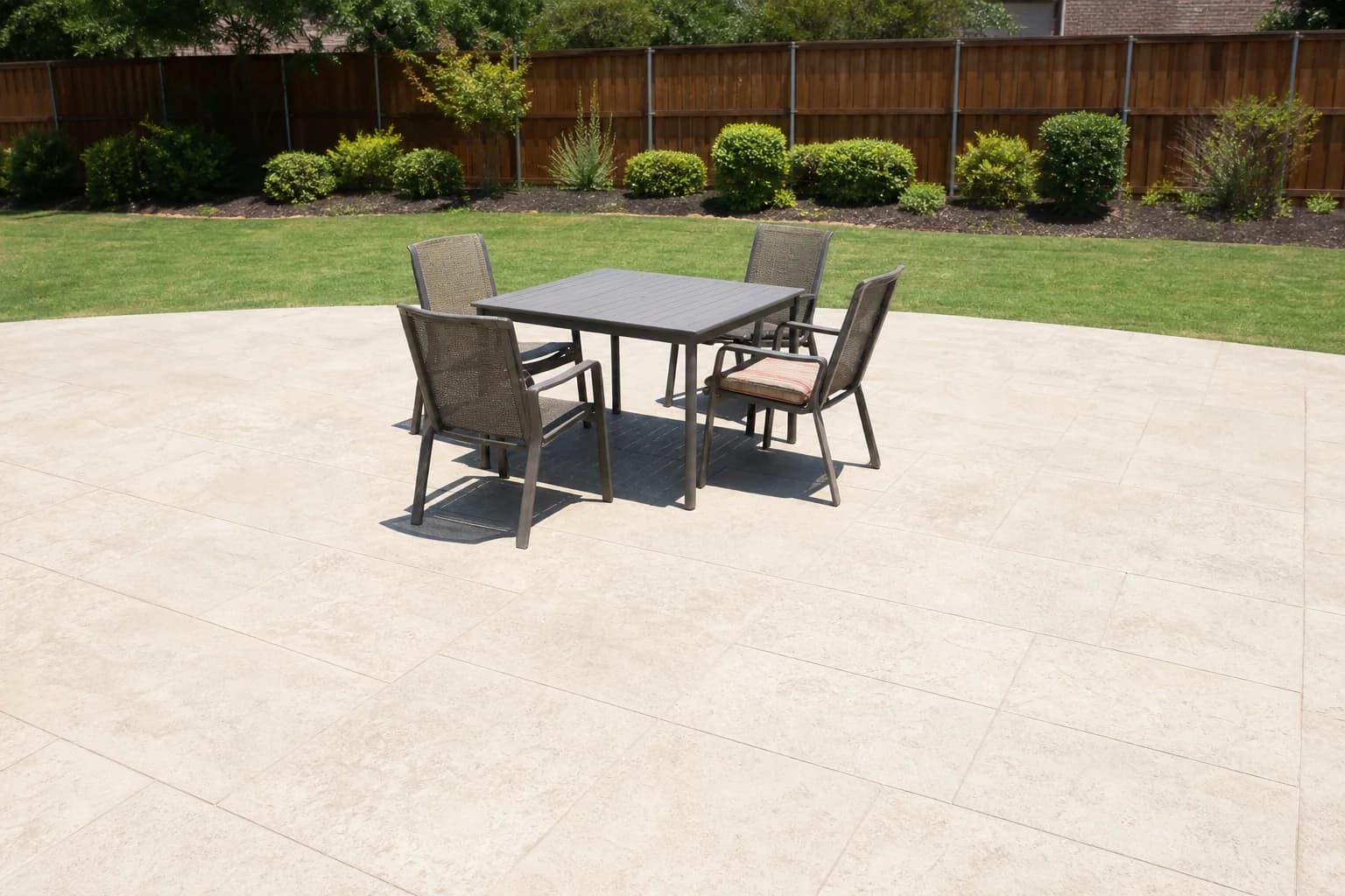 A patio table and chairs sitting unused on a bare patio in harsh overhead midday sun, with no shade over the space