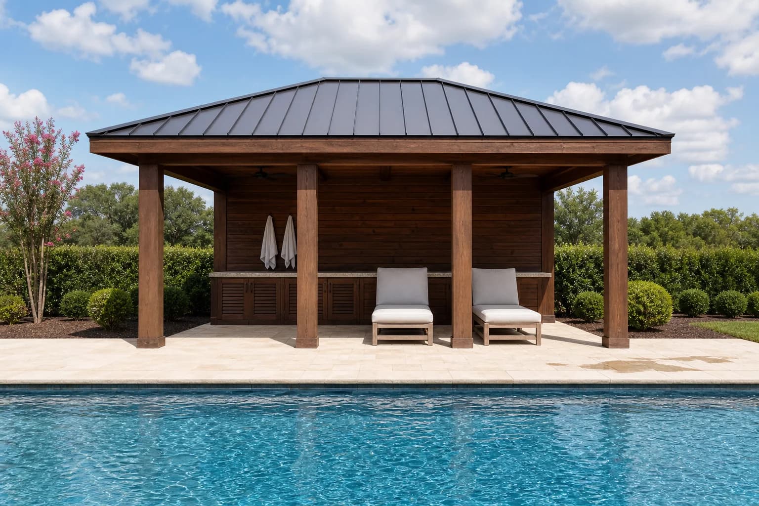 An open-air poolside cabana with a solid roof, storage doors along the back wall, and lounge chairs in its shade beside a pool