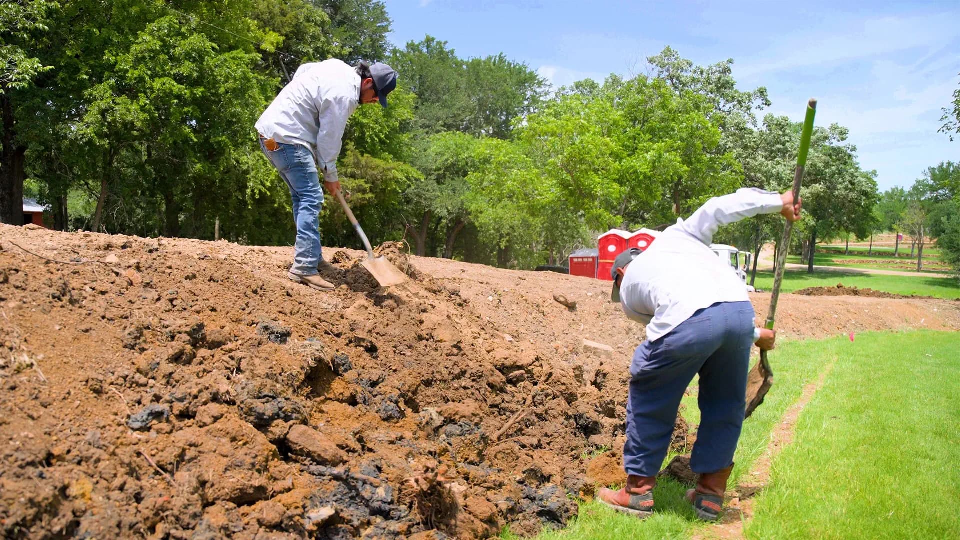 Streamline crew members grading fresh topsoil by hand with shovels