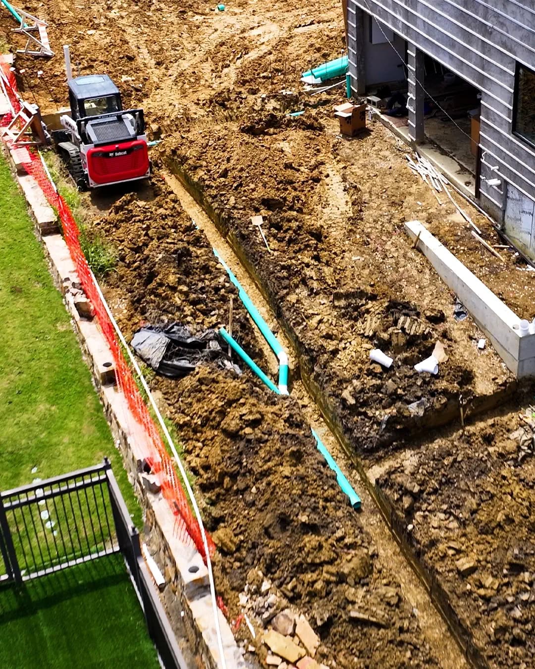 Open trench with drain pipe cut through clay soil along the side yard of a North Texas home