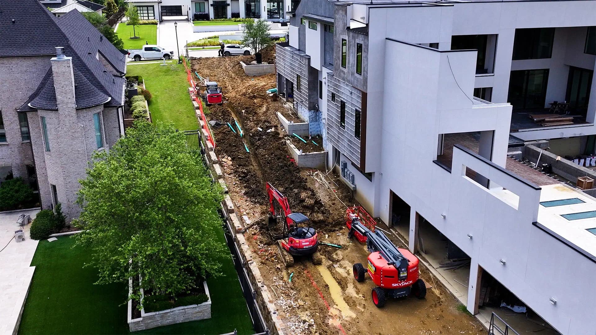 Aerial view of a large drainage installation with an excavator, skid steer, and lift equipment along a construction corridor