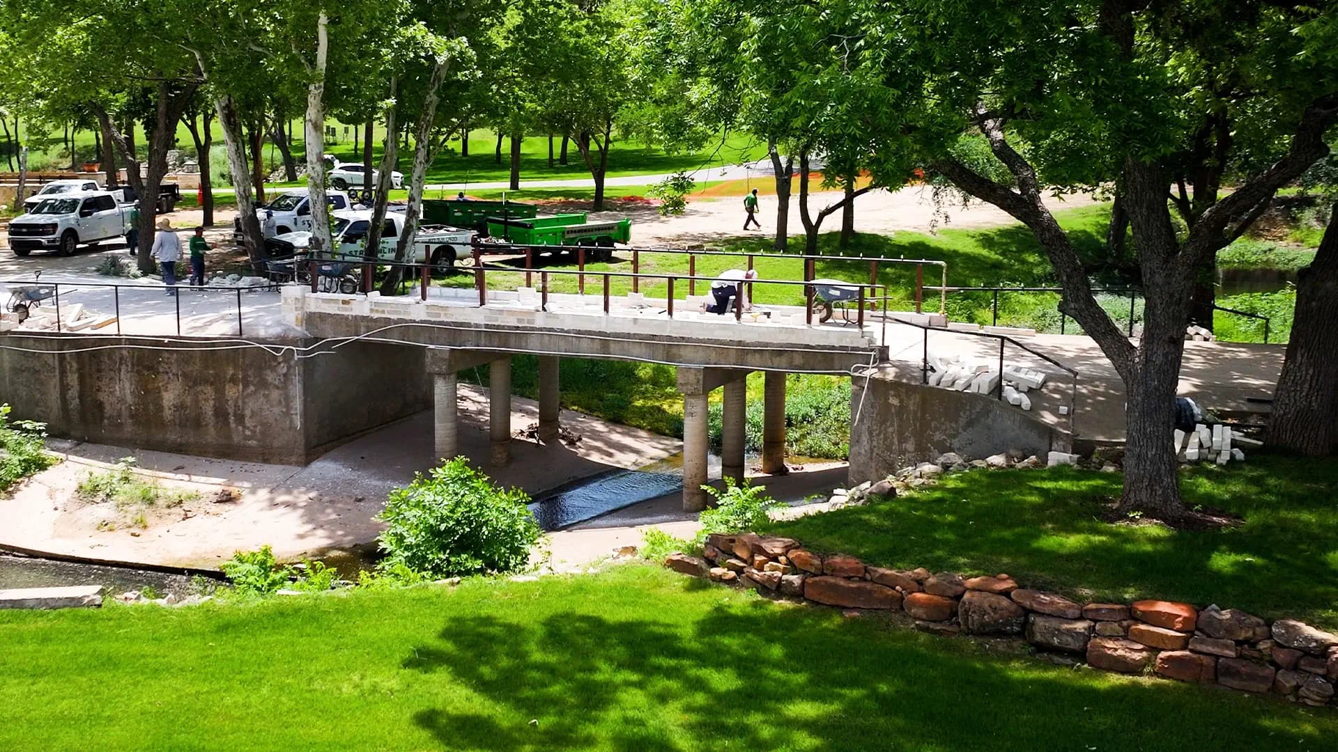 A Streamline Landscape crew laying limestone caps on a custom concrete bridge over a backyard creek