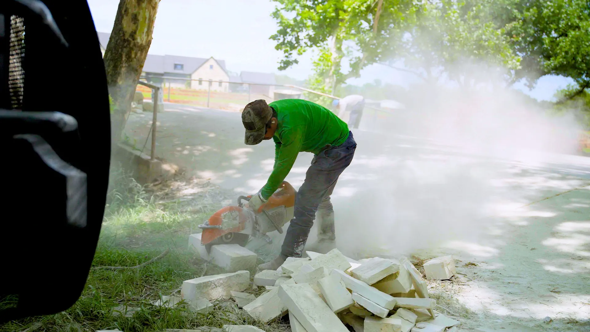 Crew member cutting limestone with a masonry saw during a hardscape installation