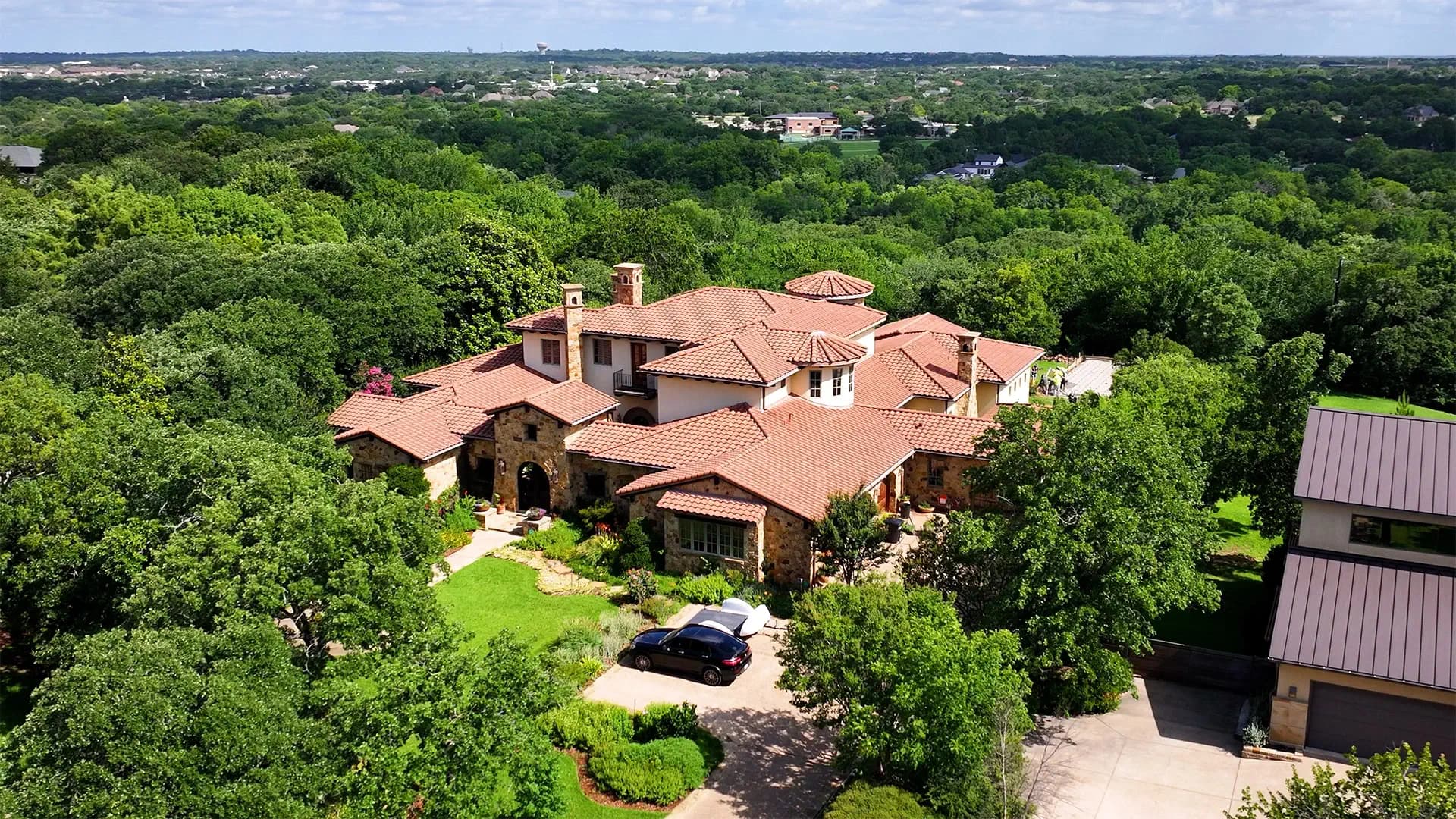 Aerial view of a stone estate home in North Texas surrounded by mature trees and layered landscape beds