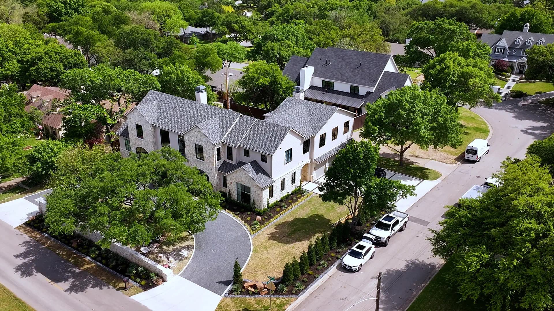 Aerial view of a full-property landscape design on a corner lot with a stone perimeter wall and cypress screening trees