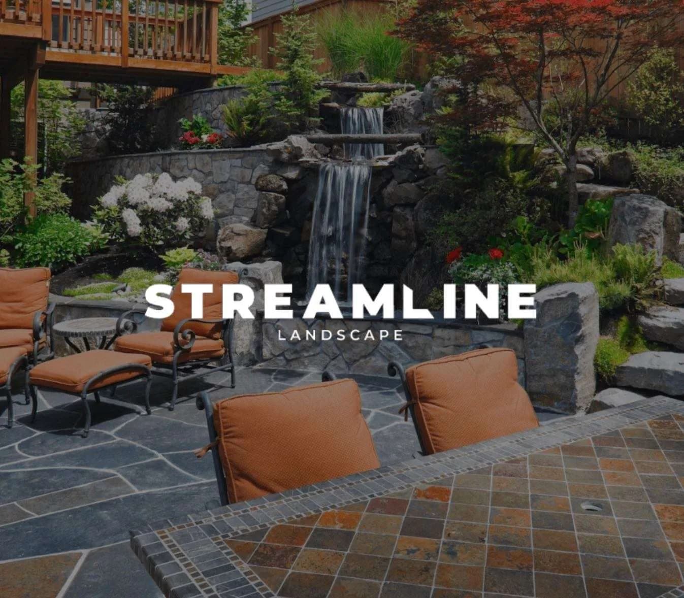 A backyard stone waterfall water feature beside a flagstone patio with cushioned seating