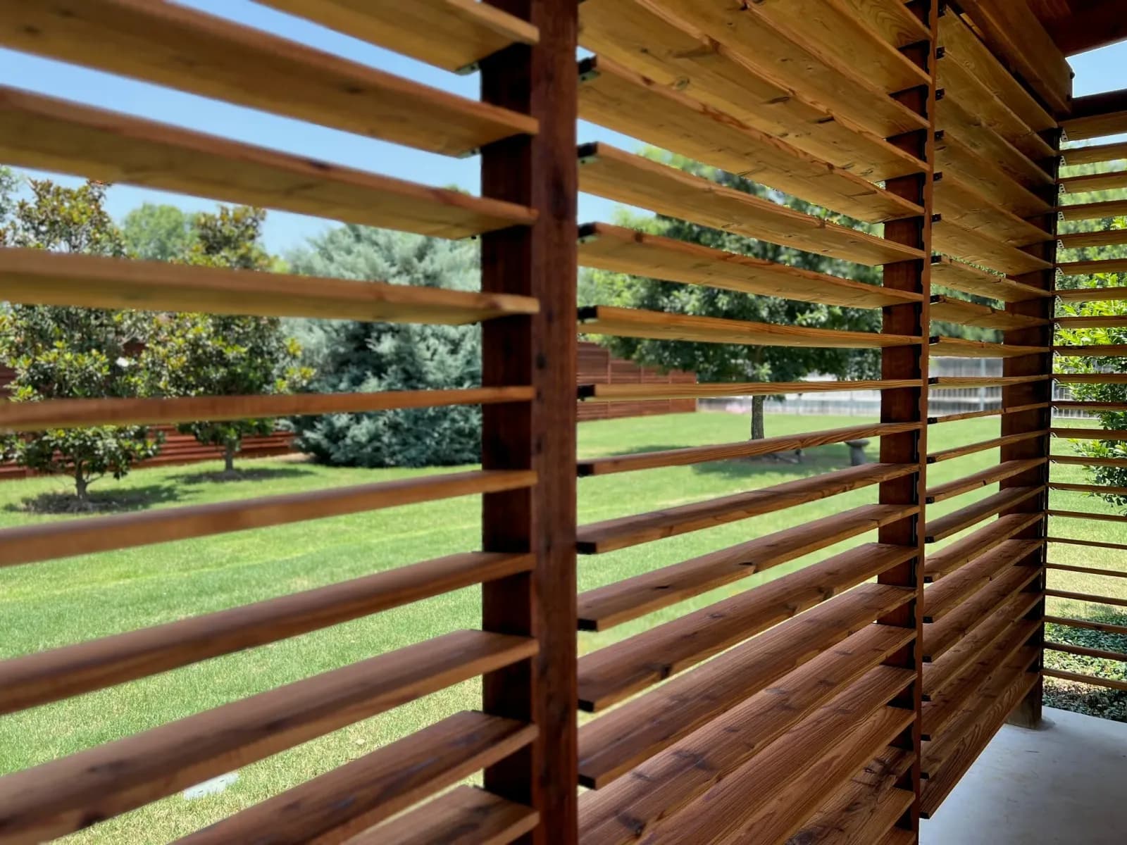 Close-up of the stained cedar louvers on a pergola screen, with a mown lawn beyond