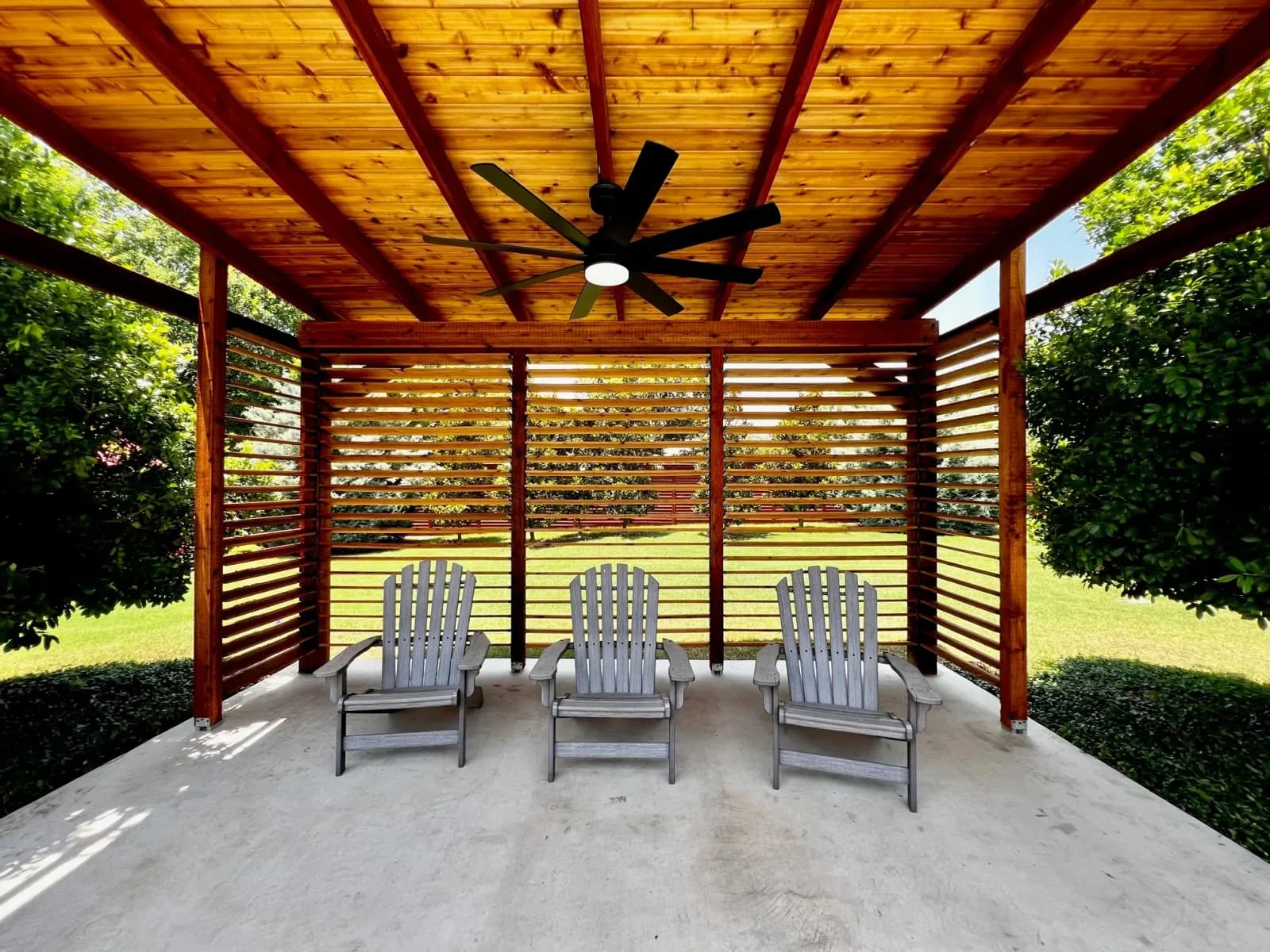 A covered cedar pergola patio with a ceiling fan and lounge seating over a stone floor
