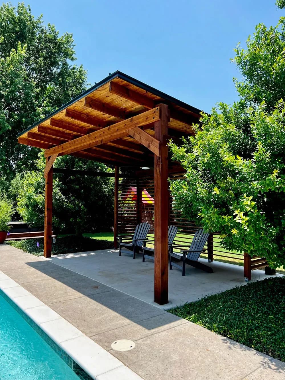 A cedar pergola shading a seating area beside a backyard pool