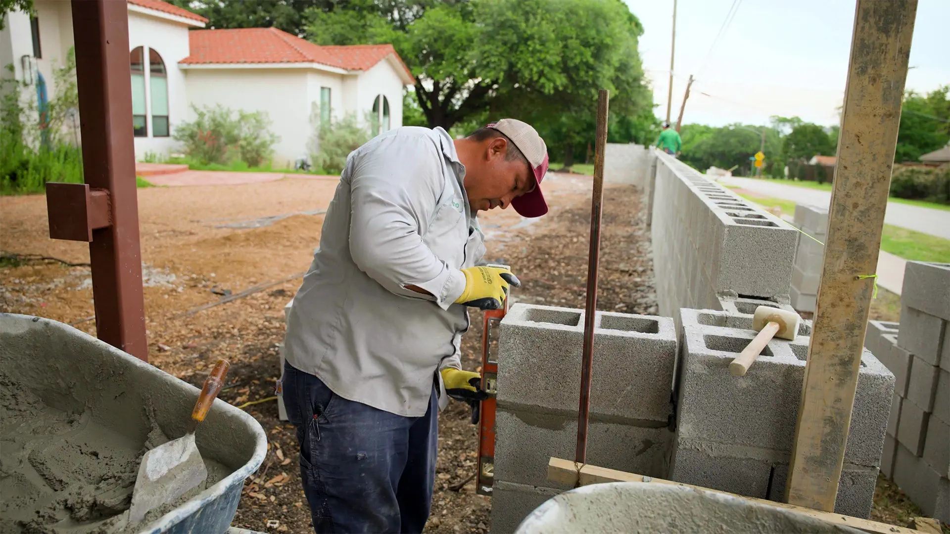 Mason checking a retaining wall column for plumb with a level as the wall run continues down the street