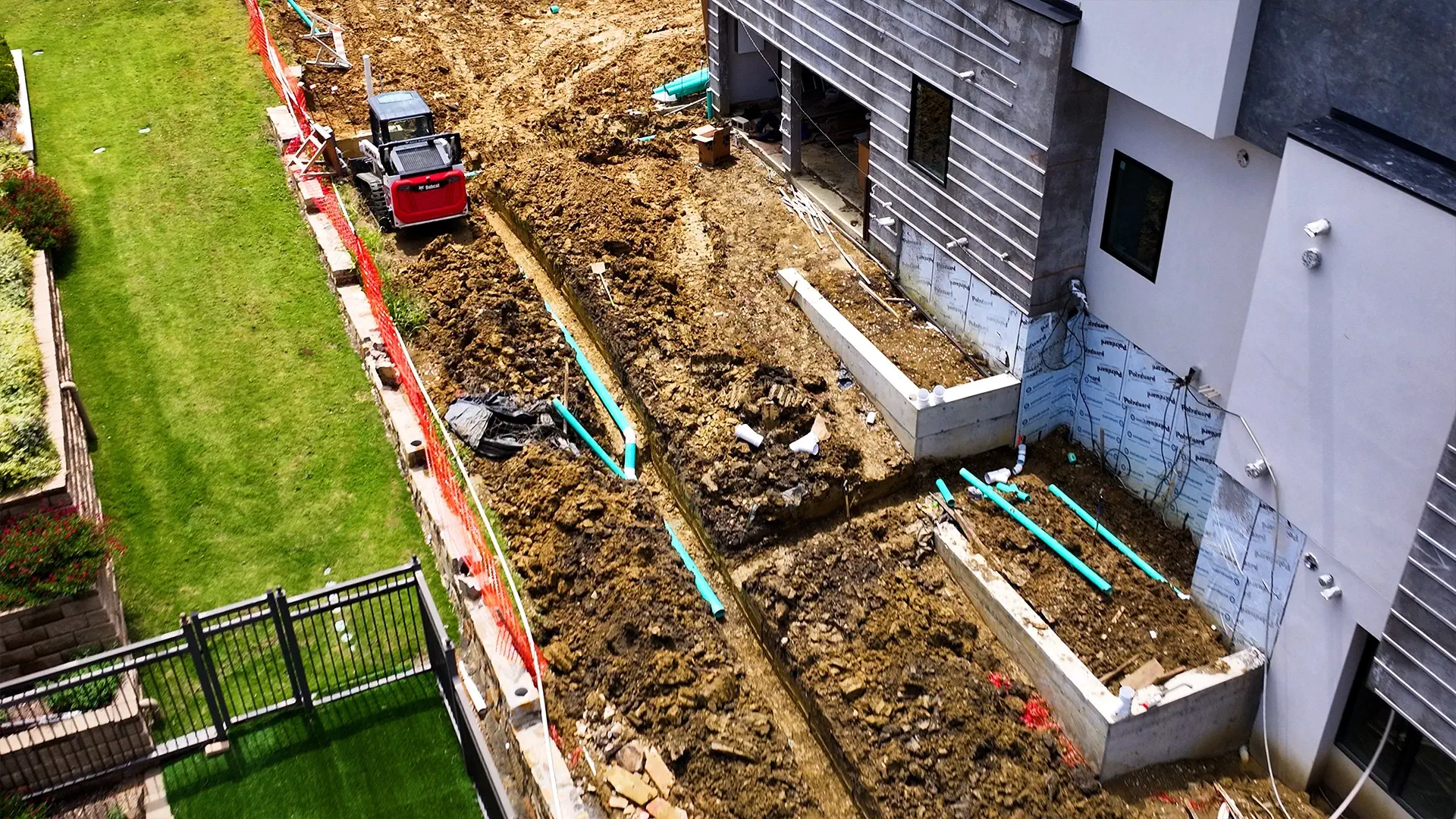 Trenched drain lines and pipe run along the side of a North Texas home during a yard drainage installation